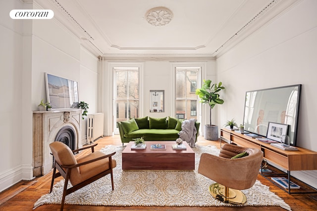 living room featuring hardwood / wood-style flooring, crown molding, a tray ceiling, and a fireplace
