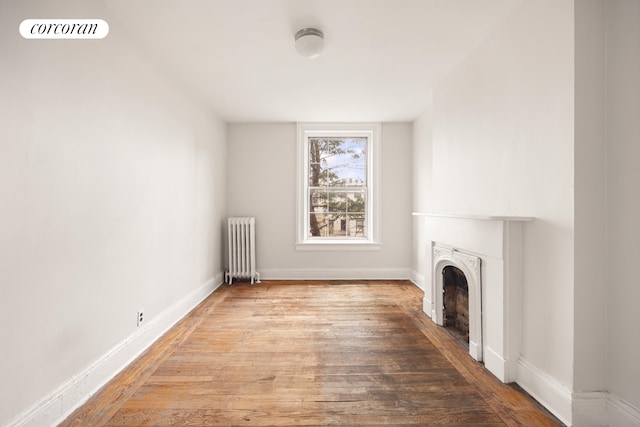 unfurnished living room with radiator heating unit, hardwood / wood-style floors, baseboards, and a fireplace