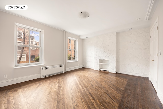 unfurnished room with radiator heating unit, wood finished floors, baseboards, and brick wall