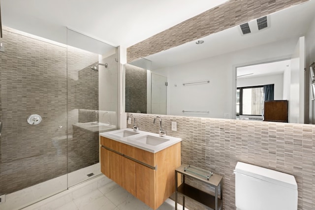 bathroom featuring tile walls, a stall shower, toilet, marble finish floors, and double vanity