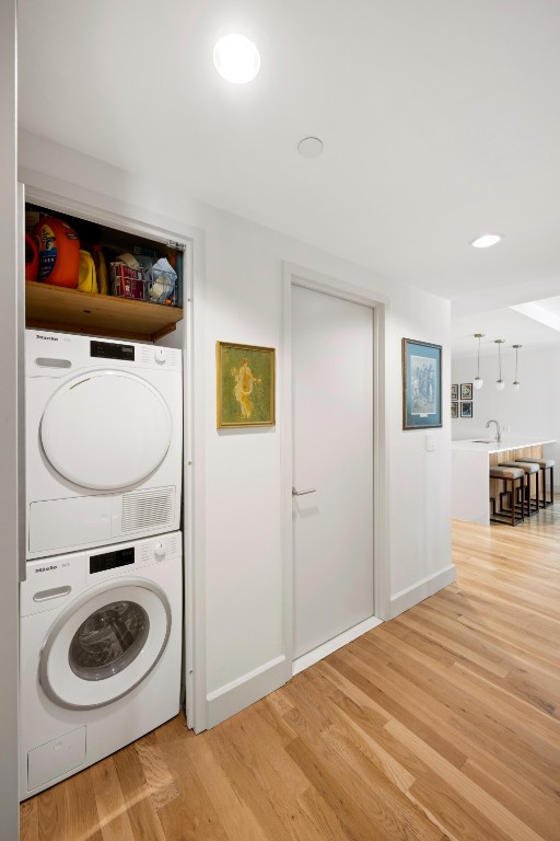 clothes washing area with laundry area, recessed lighting, stacked washer and clothes dryer, light wood-style floors, and a sink