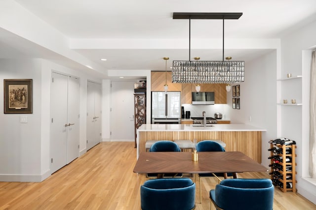 kitchen featuring stainless steel microwave, a peninsula, freestanding refrigerator, light wood finished floors, and a sink