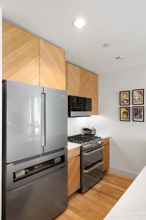 kitchen featuring baseboards, light wood finished floors, recessed lighting, stainless steel appliances, and light countertops