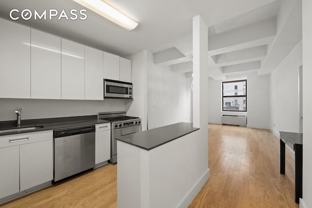 99 John St Unit 1711, New York City, NY 10038 - kitchen with stainless steel appliances, dark countertops, white cabinets, light wood-style flooring, and beam ceiling