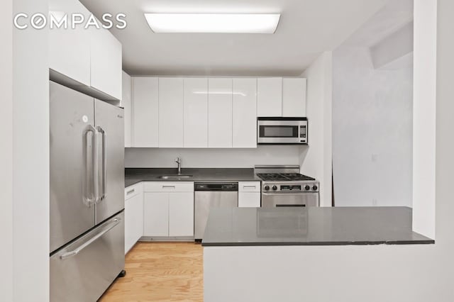 kitchen featuring light wood-type flooring, a sink, dark countertops, white cabinetry, and appliances with stainless steel finishes