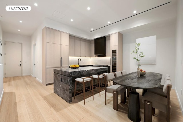 kitchen with tasteful backsplash, visible vents, a breakfast bar area, light wood-style flooring, and a kitchen island with sink