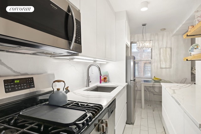 kitchen with pendant lighting, light stone counters, white cabinets, stainless steel appliances, and a sink