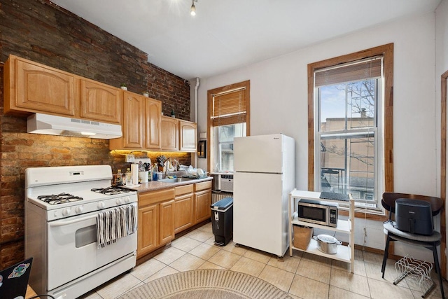 kitchen with white appliances, light tile patterned floors, light countertops, and under cabinet range hood