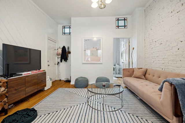 living room with light wood-style flooring, brick wall, and ornamental molding