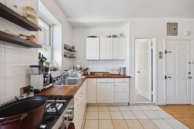 kitchen with a sink, decorative backsplash, white cabinetry, wood counters, and open shelves