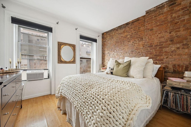 bedroom featuring cooling unit, light wood-type flooring, and brick wall