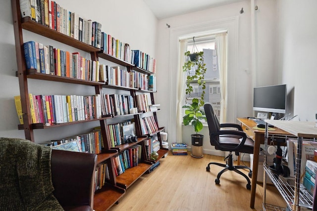 office featuring wall of books and wood finished floors