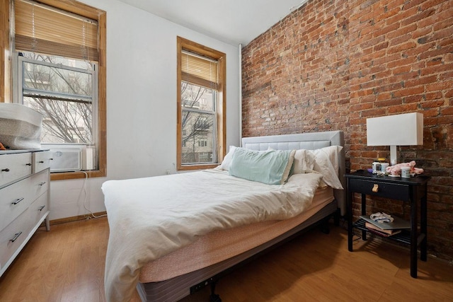 bedroom featuring cooling unit, multiple windows, brick wall, and light wood-type flooring