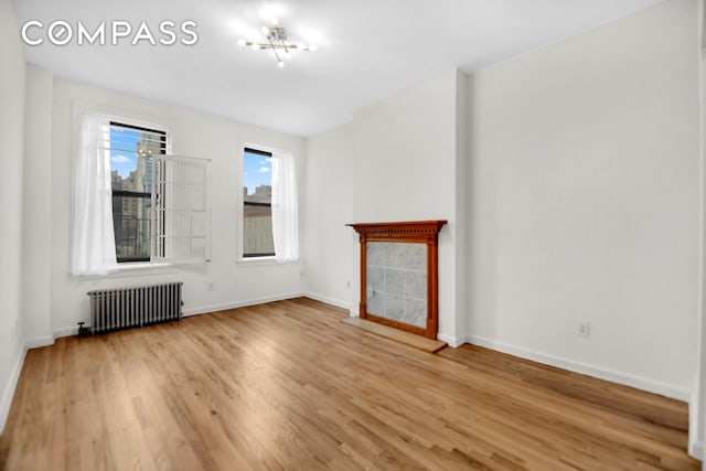 unfurnished living room featuring baseboards, radiator, and wood finished floors