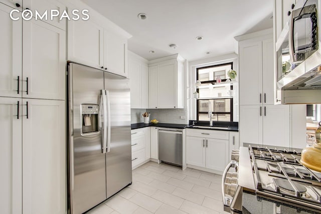 kitchen with tasteful backsplash, appliances with stainless steel finishes, white cabinetry, and dark countertops