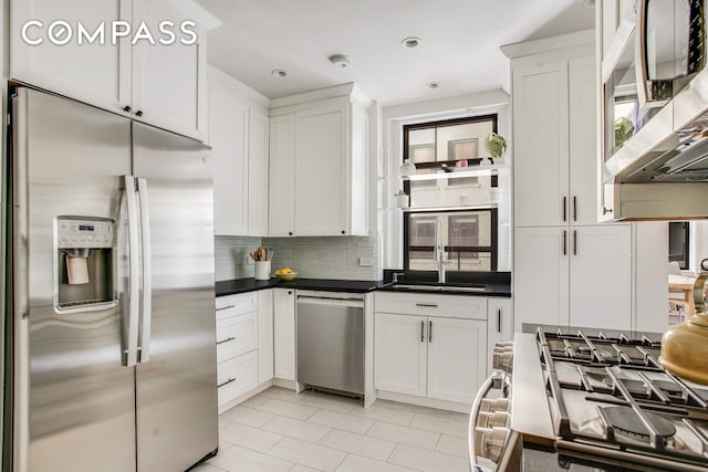 kitchen with dark countertops, a sink, decorative backsplash, light tile patterned floors, and appliances with stainless steel finishes