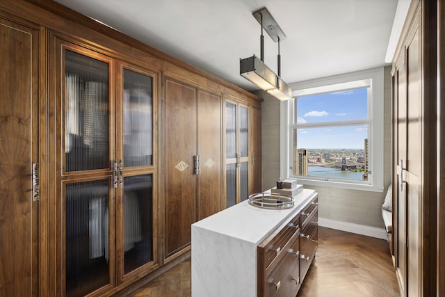 kitchen with pendant lighting, a center island, light countertops, glass insert cabinets, and baseboards