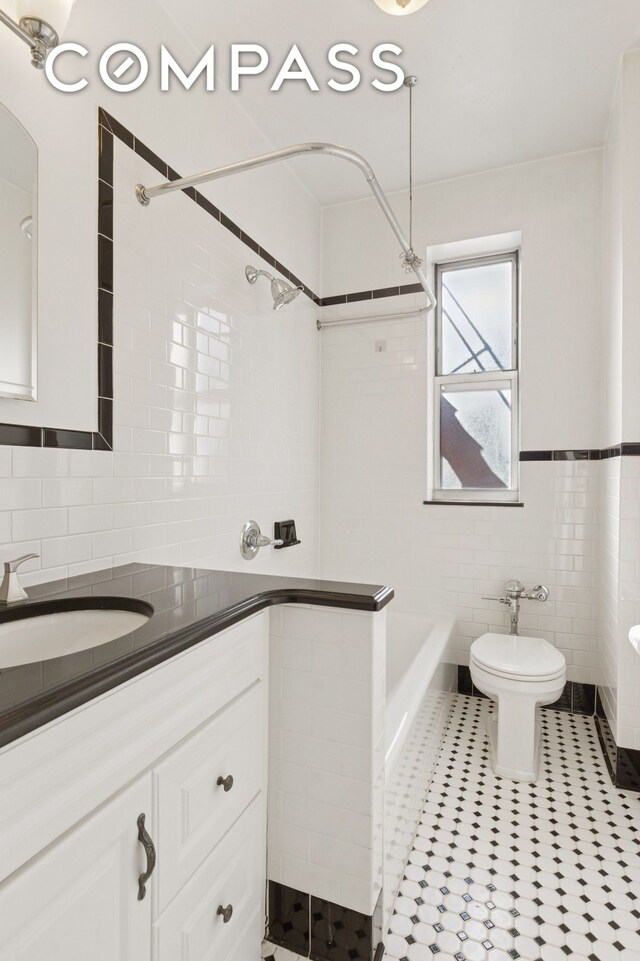 680 W 204th St Unit 5E, New York City, NY 10034 - full bath featuring tile walls, vanity, tile patterned floors, toilet, and washtub / shower combination