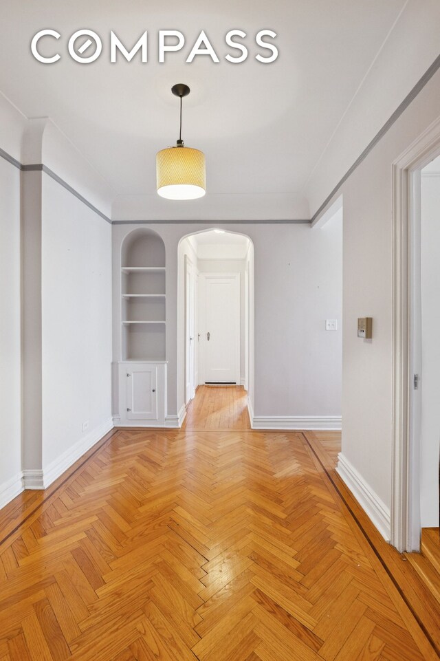 unfurnished dining area featuring arched walkways, baseboards, and built in shelves