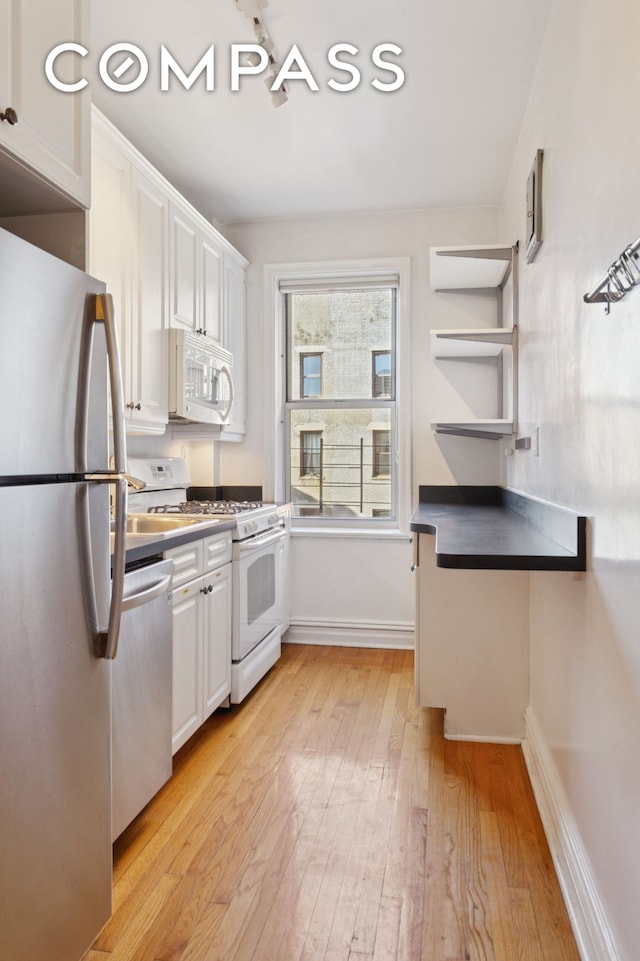 kitchen featuring light wood-style flooring, appliances with stainless steel finishes, white cabinetry, and baseboards