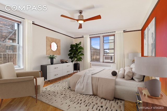 bedroom with cooling unit, radiator, a ceiling fan, and wood finished floors