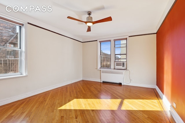 empty room featuring hardwood / wood-style floors, baseboards, radiator heating unit, cooling unit, and a ceiling fan
