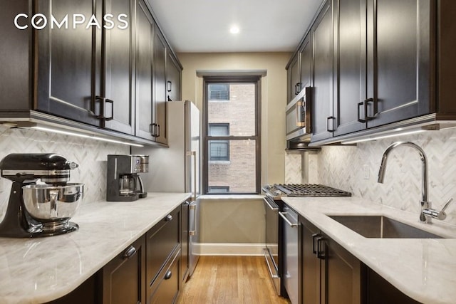 kitchen featuring light wood-type flooring, a sink, tasteful backsplash, stainless steel appliances, and light stone countertops