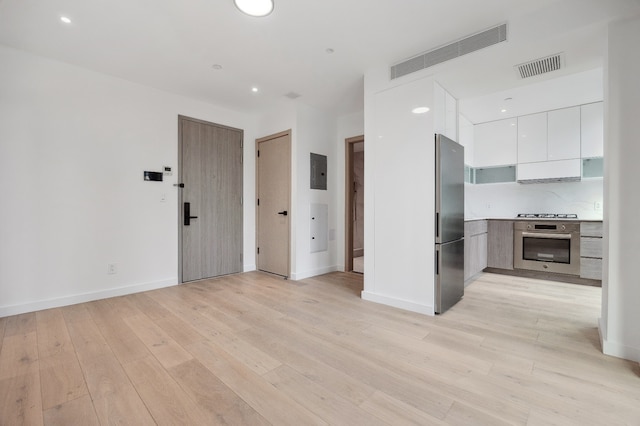 unfurnished living room featuring light wood finished floors, visible vents, baseboards, and electric panel