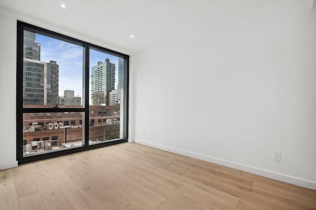 unfurnished room featuring a wall of windows, baseboards, a city view, and wood finished floors