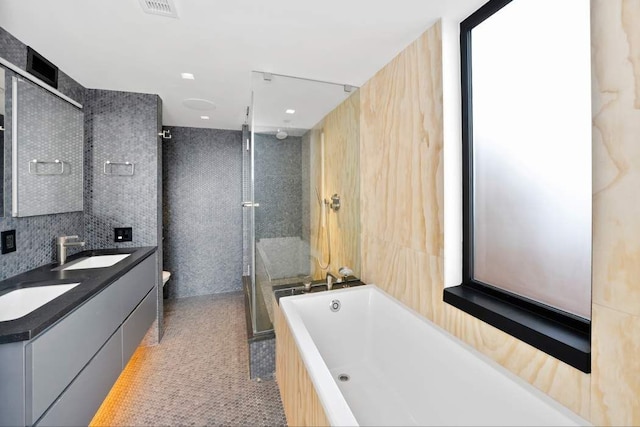 bathroom featuring visible vents, a stall shower, a bath, tile walls, and a sink