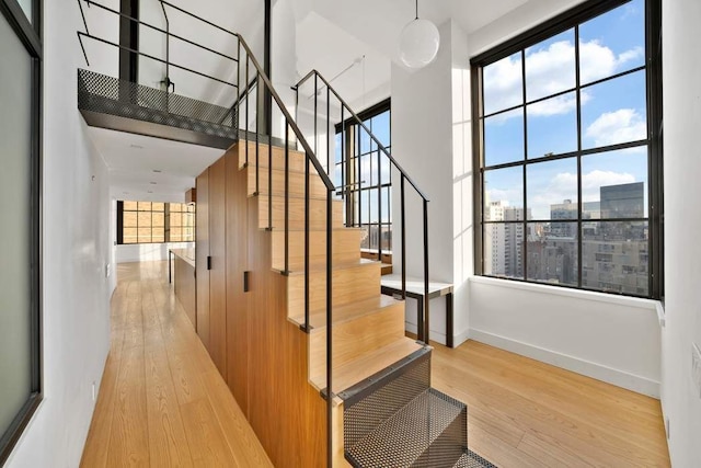 stairway with a view of city, a high ceiling, baseboards, and wood finished floors