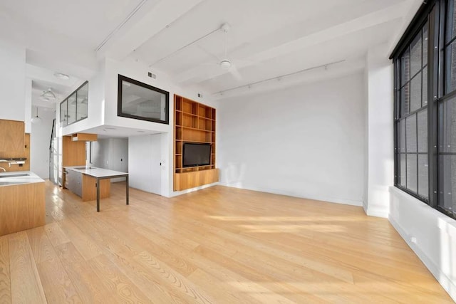 unfurnished living room with a ceiling fan, baseboards, a sink, rail lighting, and light wood-type flooring