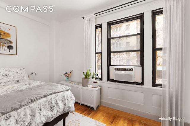 bedroom featuring a decorative wall, cooling unit, and light wood-style floors