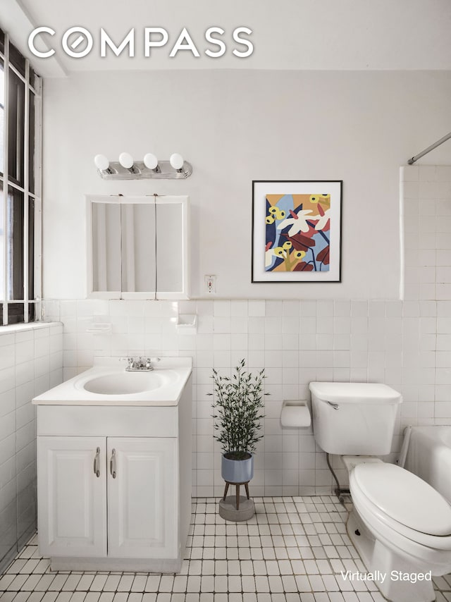 full bath with tile patterned floors, toilet, tile walls, wainscoting, and vanity