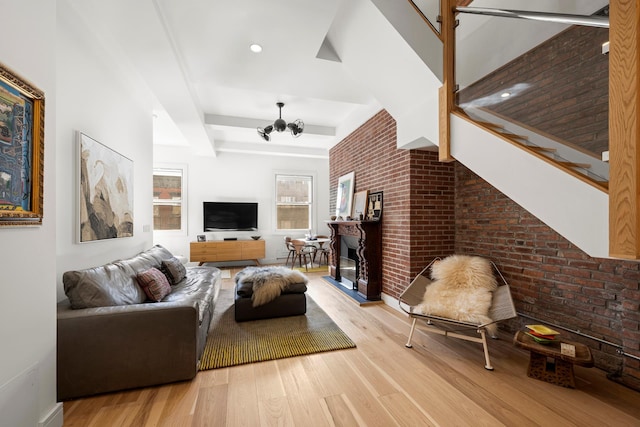 living room featuring a notable chandelier, brick wall, a glass covered fireplace, and wood finished floors