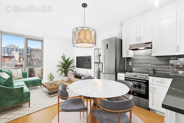 kitchen featuring under cabinet range hood, dark countertops, light wood-type flooring, and appliances with stainless steel finishes