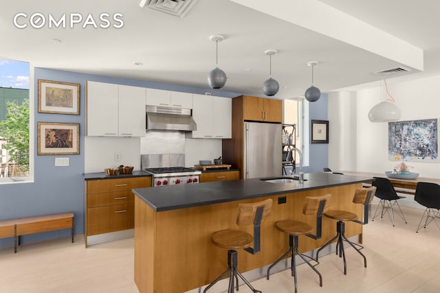 kitchen with visible vents, under cabinet range hood, high end refrigerator, white cabinetry, and a sink