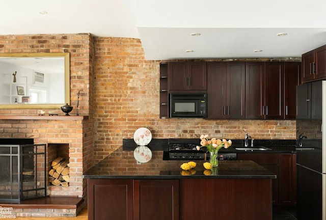 kitchen with a sink, dark stone countertops, black microwave, dark brown cabinets, and a brick fireplace