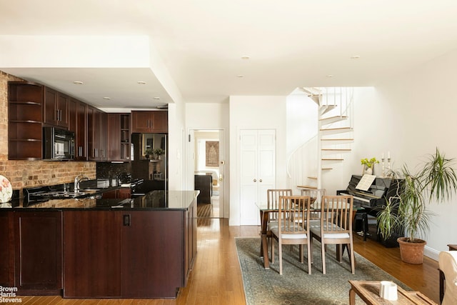 kitchen with wood finished floors, a peninsula, open shelves, black microwave, and fridge