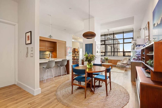 dining space featuring baseboards, light wood-type flooring, and a high ceiling