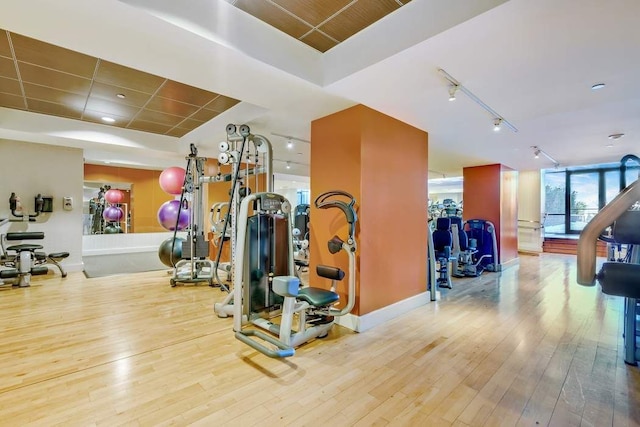 gym featuring track lighting, baseboards, and hardwood / wood-style flooring