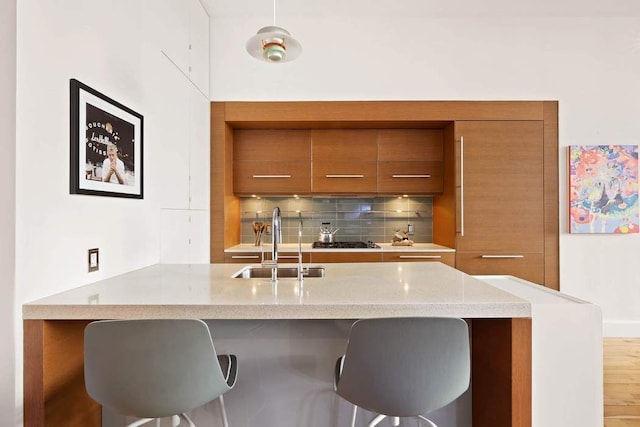 kitchen with brown cabinets, modern cabinets, a sink, backsplash, and a breakfast bar area