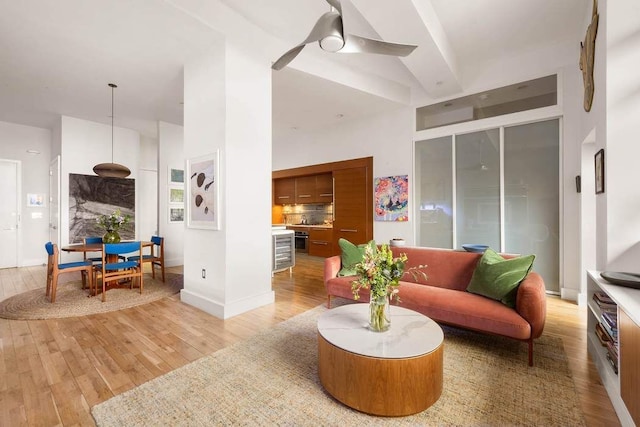 living area with a high ceiling, baseboards, light wood-type flooring, and ceiling fan