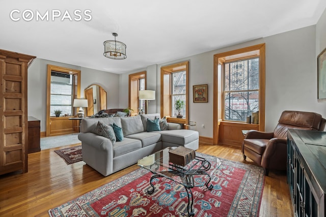 living room with an AC wall unit, baseboards, an inviting chandelier, and light wood finished floors