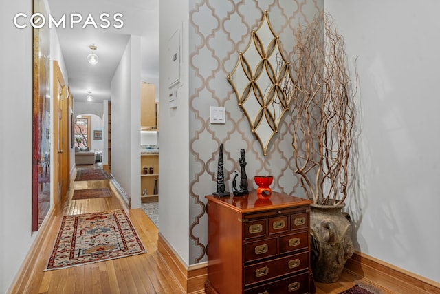 corridor with baseboards, arched walkways, and light wood finished floors