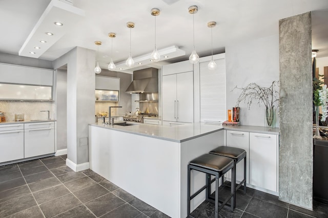 kitchen with modern cabinets, a peninsula, white cabinets, and wall chimney range hood