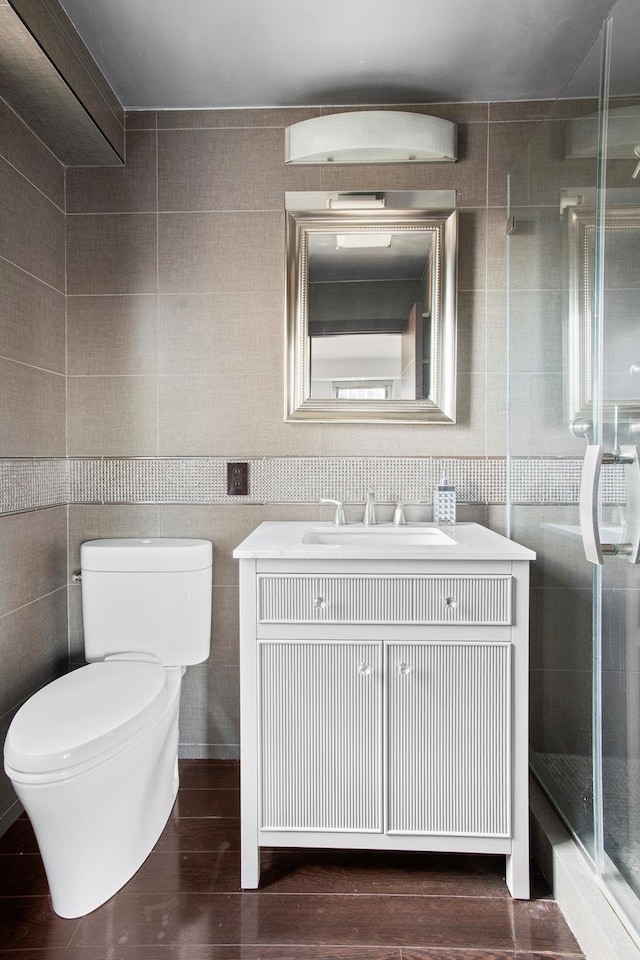 bathroom with toilet, vanity, a stall shower, wood finished floors, and tile walls