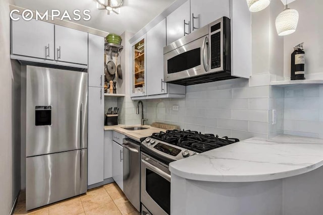 kitchen with light stone countertops, light tile patterned floors, decorative backsplash, appliances with stainless steel finishes, and a sink