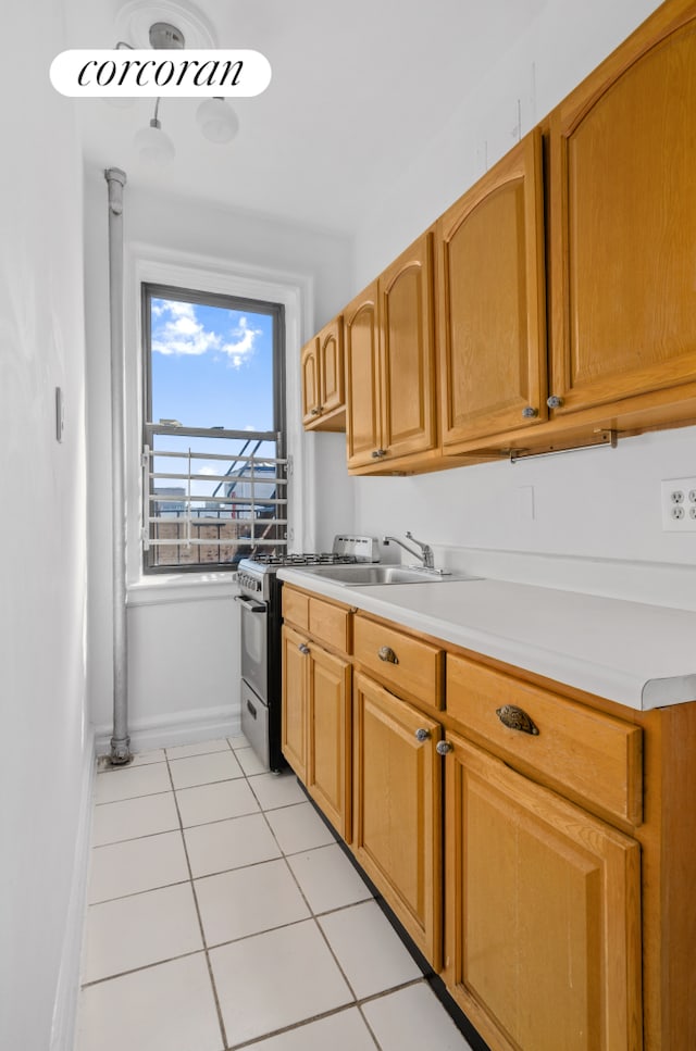 kitchen with a sink, light tile patterned flooring, light countertops, baseboards, and stainless steel gas range