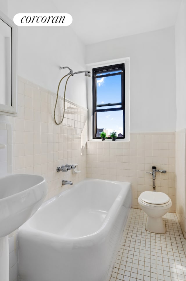 full bath with toilet, a tub to relax in, wainscoting, tile patterned floors, and tile walls